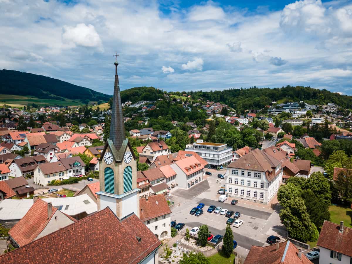 Dorfplatz mit katholischer Kirche und Gemeindehaus von Westen gesehen. Drohnenfoto.