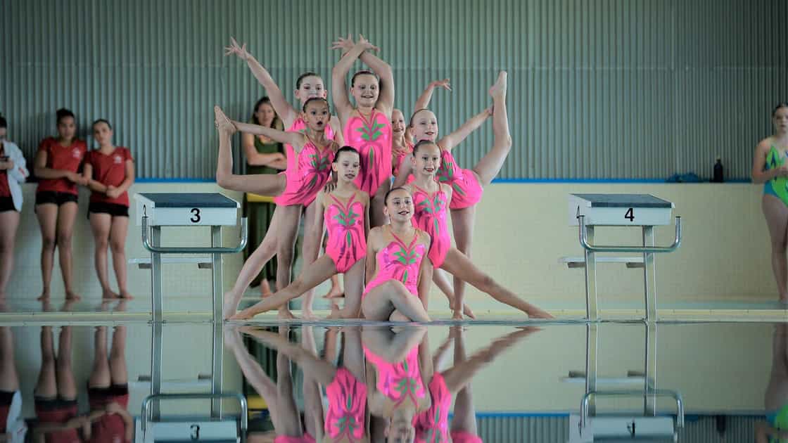 L'image représente la pose de départ de l'équipe avant le début de la chorégraphie. Les huit nageuses portent un maillot de bain rose, et portent toutes un chignon avec de la gélatine sur la tête. La gélatine sert à garder les cheveux plaqués lors de la performance aquatique.