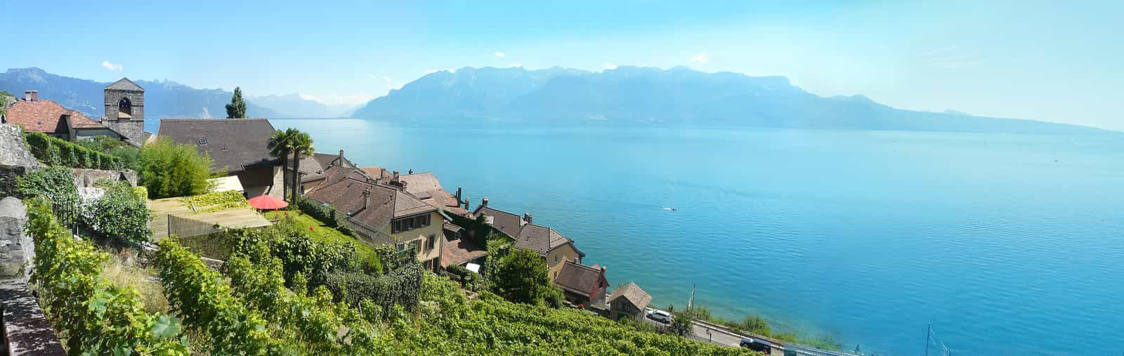 Das Schweizer Dorf Saint-Saphorin und sein protestantischer Tempel, umgeben von den Hängen des Lavaux, am Ufer des Genfer Sees westlich von Vevey, gegenüber dem nördlichen Ende der französischen Alpen (vorne und rechts).