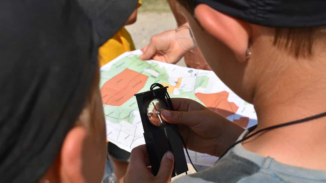 Kinder orientieren sich mit einem Kompass und einer Karte.
