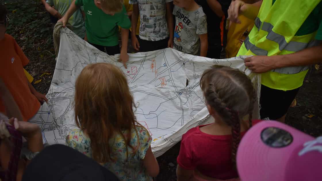 Kinder suchen auf einer in Stoff gezeichneten Karte nach einem Schatz.