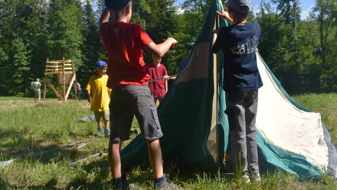 Zwei Kinder bauen ein Zelt auf einem Lagerplatz auf.